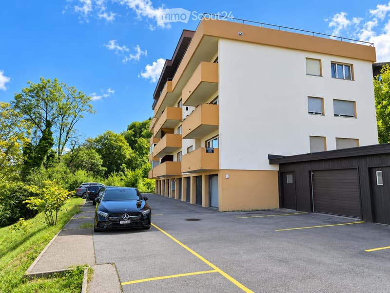 Modern multi-story apartment building with balconies, garage, and parking area.