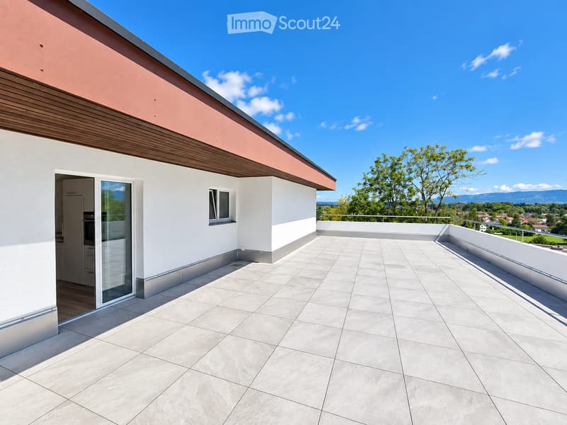 Modern rooftop terrace with large tiled floor, white walls, and a metal railing, offering a scenic view of the surrounding landscape and mountains.