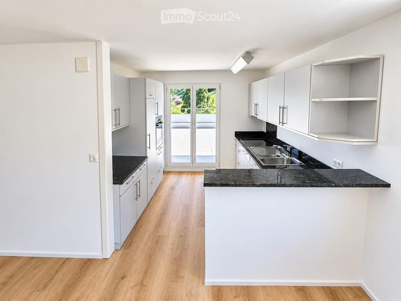 Modern kitchen with white cabinets, black countertops, and a central island. Features a wooden floor and large windows with a view of the garden.