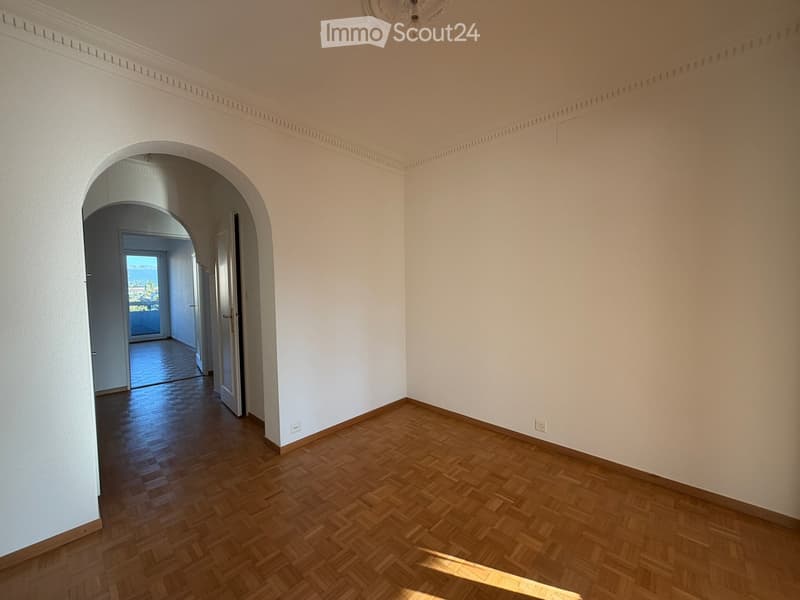 Empty room with wooden flooring, white walls, and an arched doorway leading to another room with a view of the outdoors.