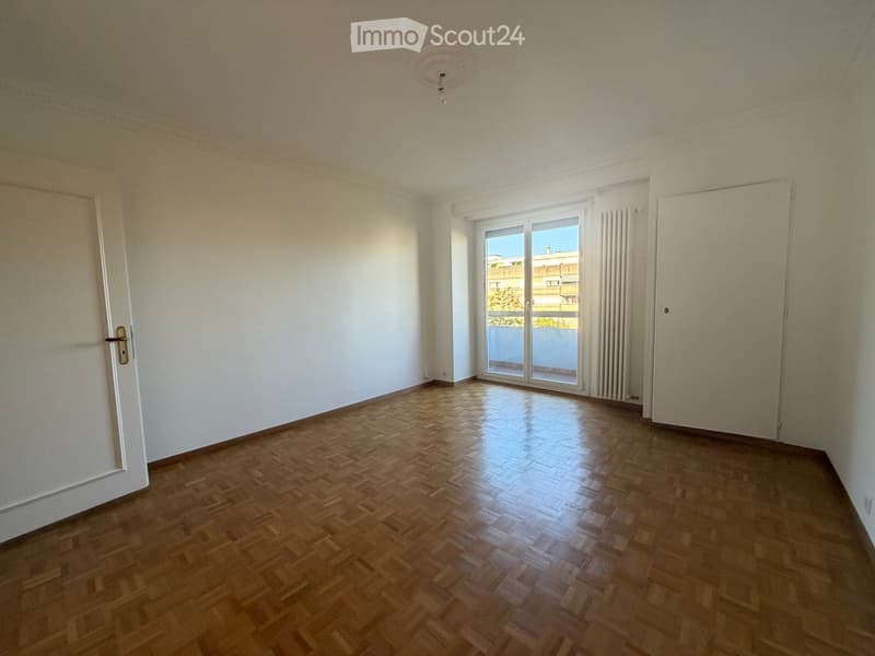 Empty room with wooden parquet flooring, white walls, and large sliding glass doors leading to a balcony.