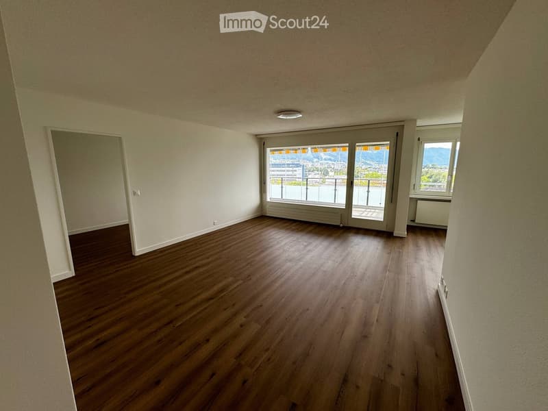 Empty room with wooden flooring, large windows, and a sliding glass door leading to a balcony.