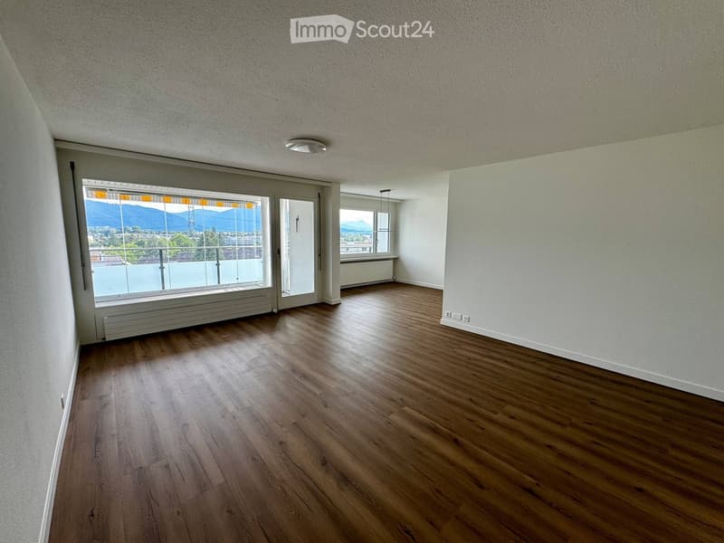 Empty room with wooden flooring, white walls, large windows, and a sliding glass door leading to a balcony with a scenic mountain view.