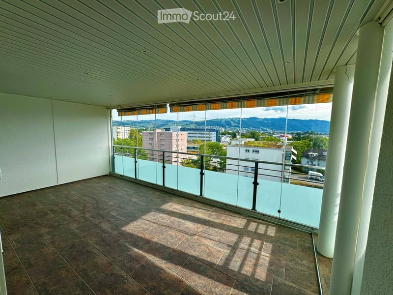 Balcony with tiled floor, glass railing, and a view of the city and mountains.