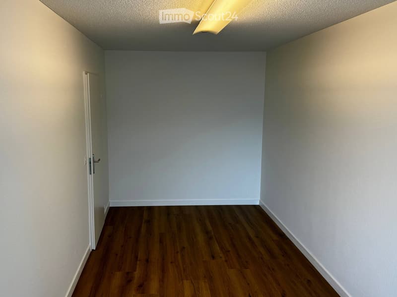 Empty room with wooden flooring, white walls, and a single door on the left side.