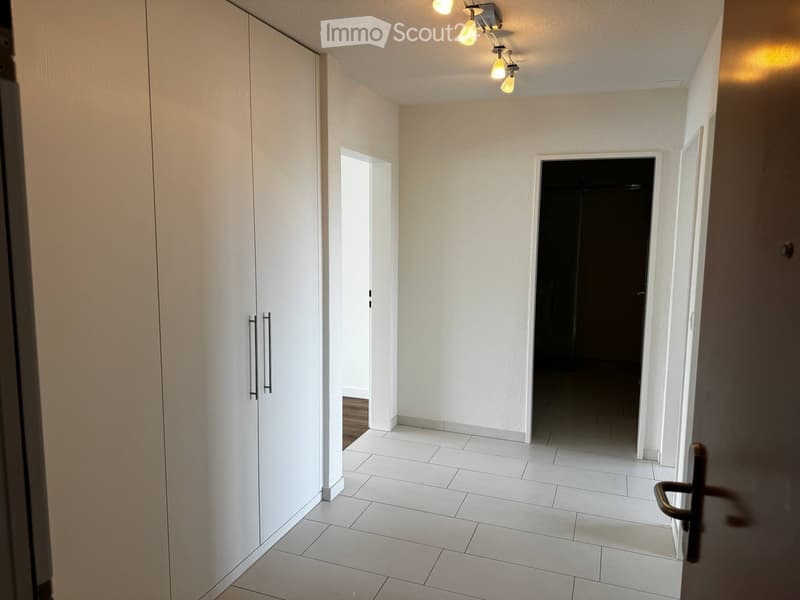 Empty hallway with white tiled flooring, white walls, and a built-in white closet on the left side. The hallway has two open doorways leading to other rooms.