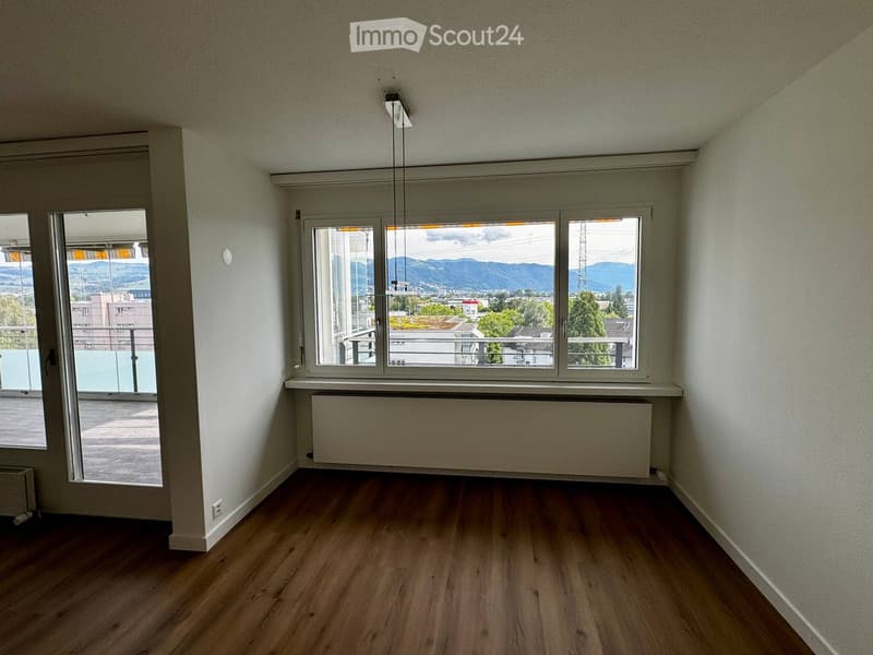 Empty room with wooden flooring, white walls, large windows offering a scenic view, and a radiator below one window.
