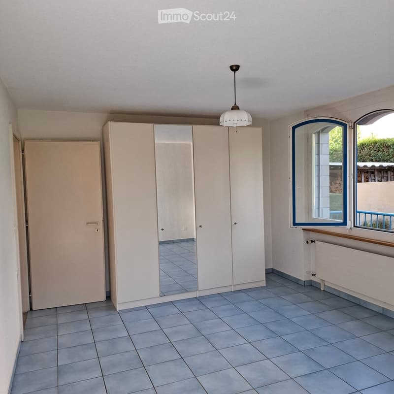 Empty room with tiled floor, white walls, large mirrored wardrobe, and two windows with blue frames.