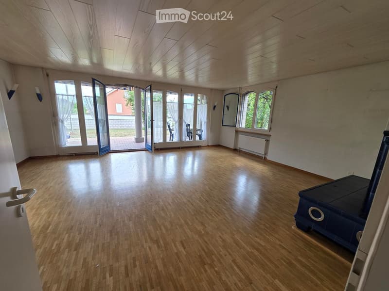 Empty room with wooden flooring, large windows with white curtains, and a sliding glass door leading to an outdoor area.
