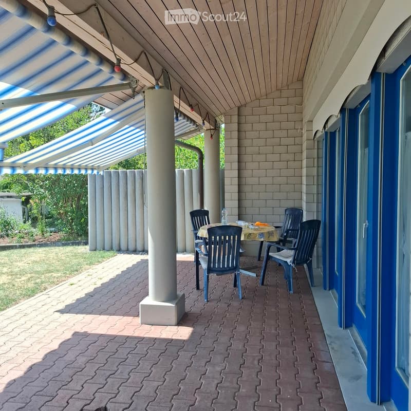 Balcony with a striped awning, brick floor, and a small table with chairs.