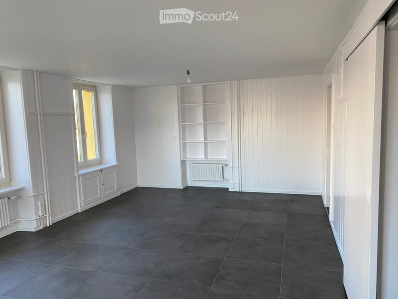 Empty room with white walls, dark tiled floor, built-in shelving unit, and window with radiator below.