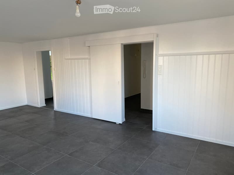 Empty room with white paneled walls, dark tiled floor, and two open doorways leading to other spaces.