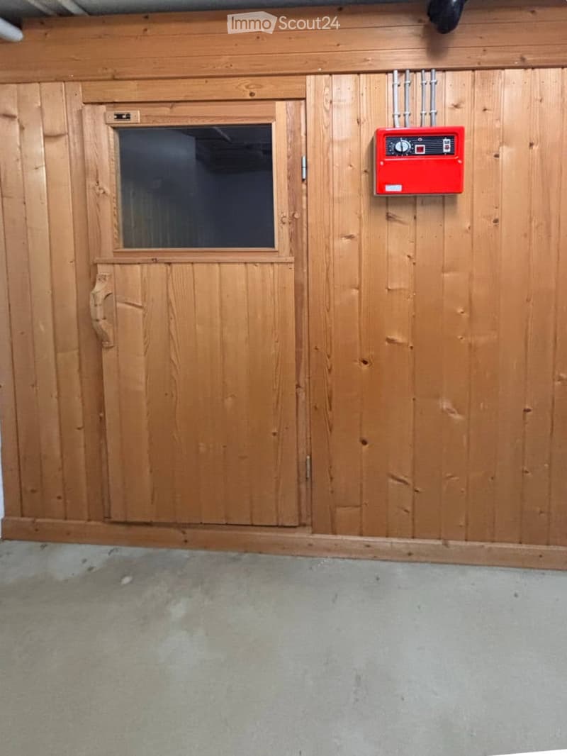 Empty room with wooden panel walls, a small window, and a red fire alarm box mounted on the wall.