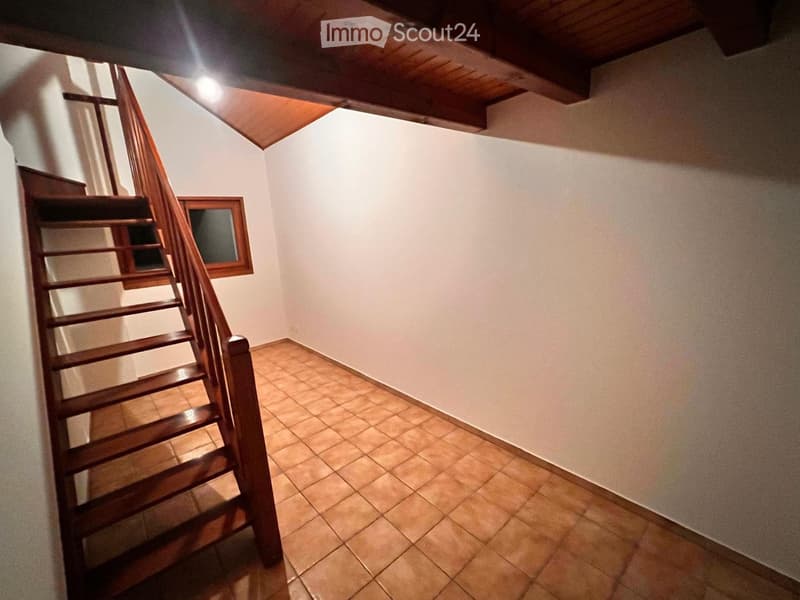 Empty hallway with wooden staircase, tiled floor, and white walls.