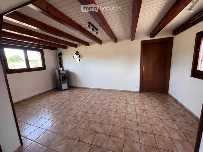 Empty room with exposed wooden beams on the ceiling, tiled floor, and a small wood-burning stove in the corner.