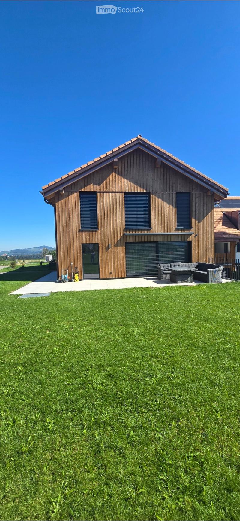 Modern two-story house with wooden exterior, large windows, garage, and outdoor seating area with sofa and table.