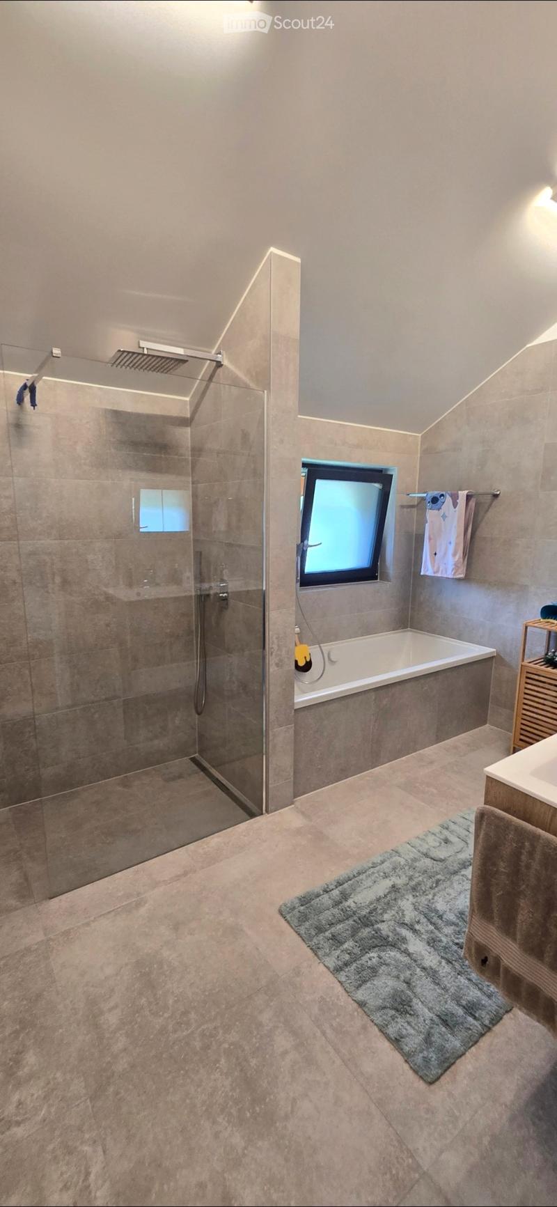 Modern bathroom with a bathtub, walk-in shower, large window, towel rack, and a small sink area.