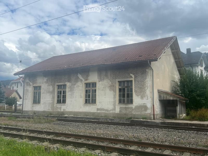 Two-story brick building with a red-tiled roof, multiple windows, and a small garage attached. Located near railway tracks.