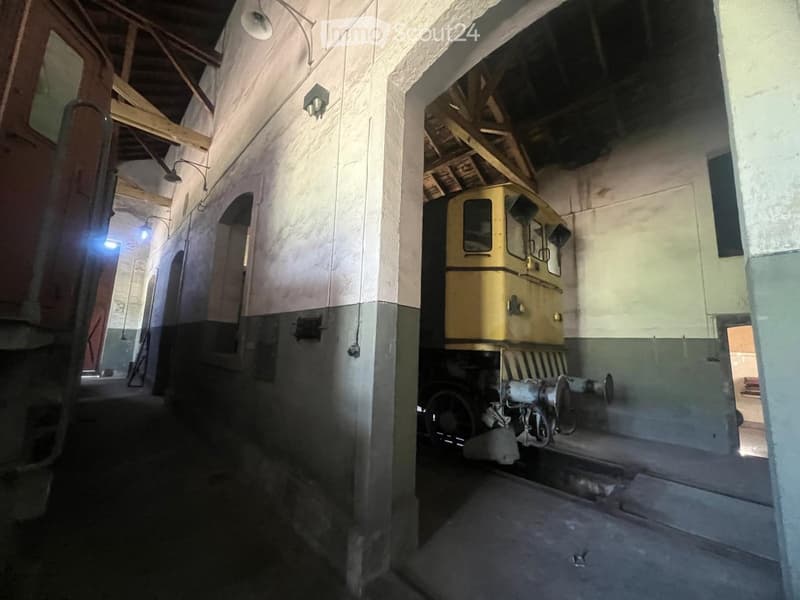 A large industrial space with a train on the left and machinery on the right, featuring exposed wooden beams and concrete floors.