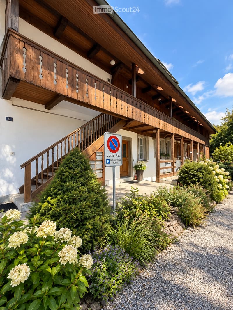 Two-story wooden house with a balcony, white exterior, and well-maintained garden with flowers and shrubs.