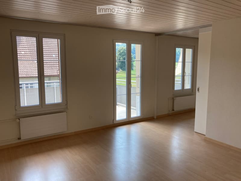 Empty room with wooden flooring, large windows, radiators, and a sliding glass door leading to a balcony.