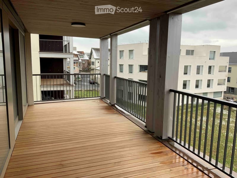 Balcony with wooden decking, metal railing, and view of surrounding buildings and greenery.