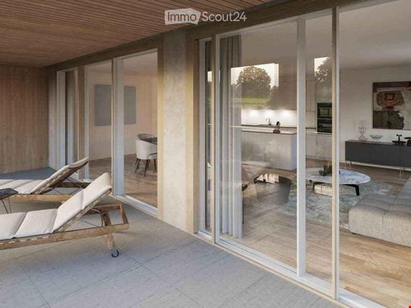 Modern, well-lit living space with large glass sliding doors connecting to a patio. The living area features a white sofa, coffee table, and a dining area with chairs and a table. The kitchen area includes cabinets, a faucet, and an oven. A mirror and an