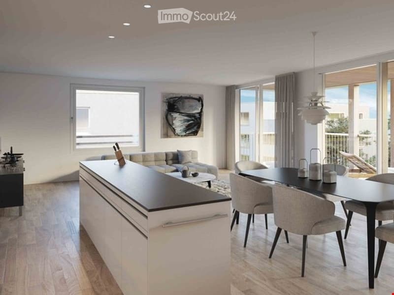 Modern, open-plan living and dining area with a white kitchen island, grey sofa, dining table with chairs, and large windows leading to a balcony.