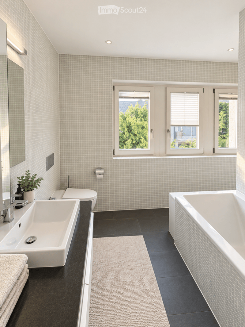 Modern bathroom with white tiles, black flooring, a large window, a sink with a faucet, a toilet, a bathtub, a mirror, and a small plant on the counter.