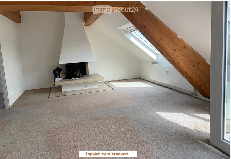 Empty attic room with exposed wooden beams, skylight window, fireplace, and carpeted floor.