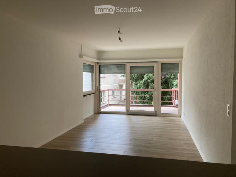 Empty room with wooden flooring, large sliding glass doors leading to a balcony, and a window on the left side.