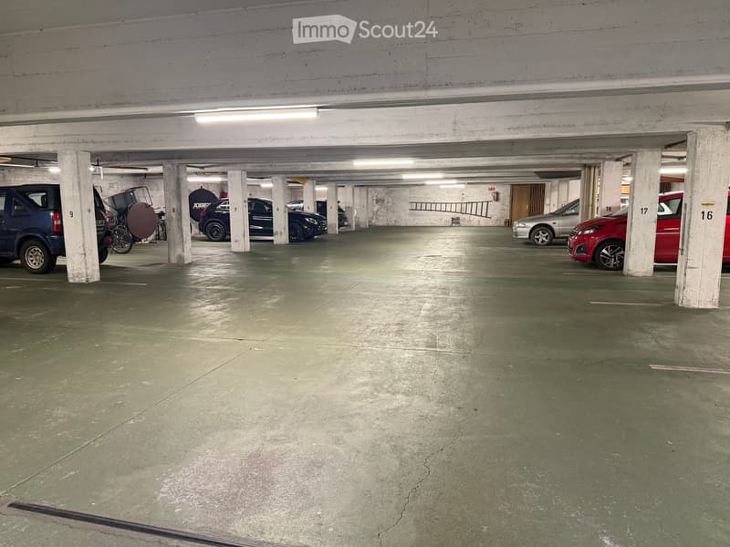 Underground parking area with several parked cars, concrete pillars, and numbered parking spaces.