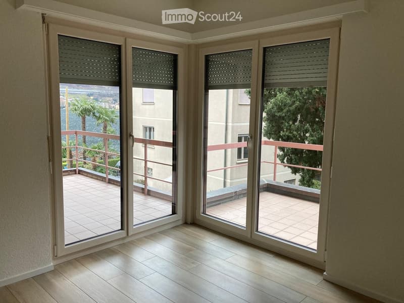 Empty room with large sliding glass doors opening to a tiled balcony with a view of water and trees.
