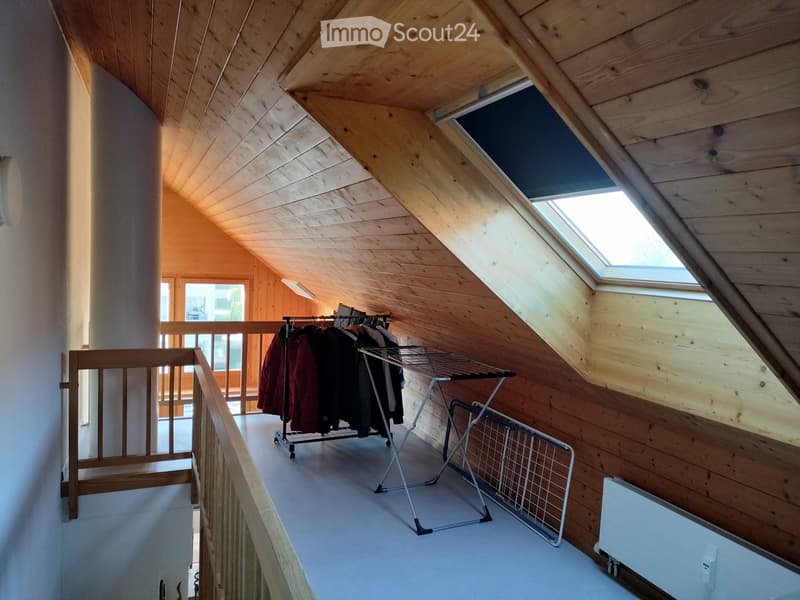 Attic room with wooden walls and ceiling, skylight windows, clothing rack, radiator, and staircase leading to another area.