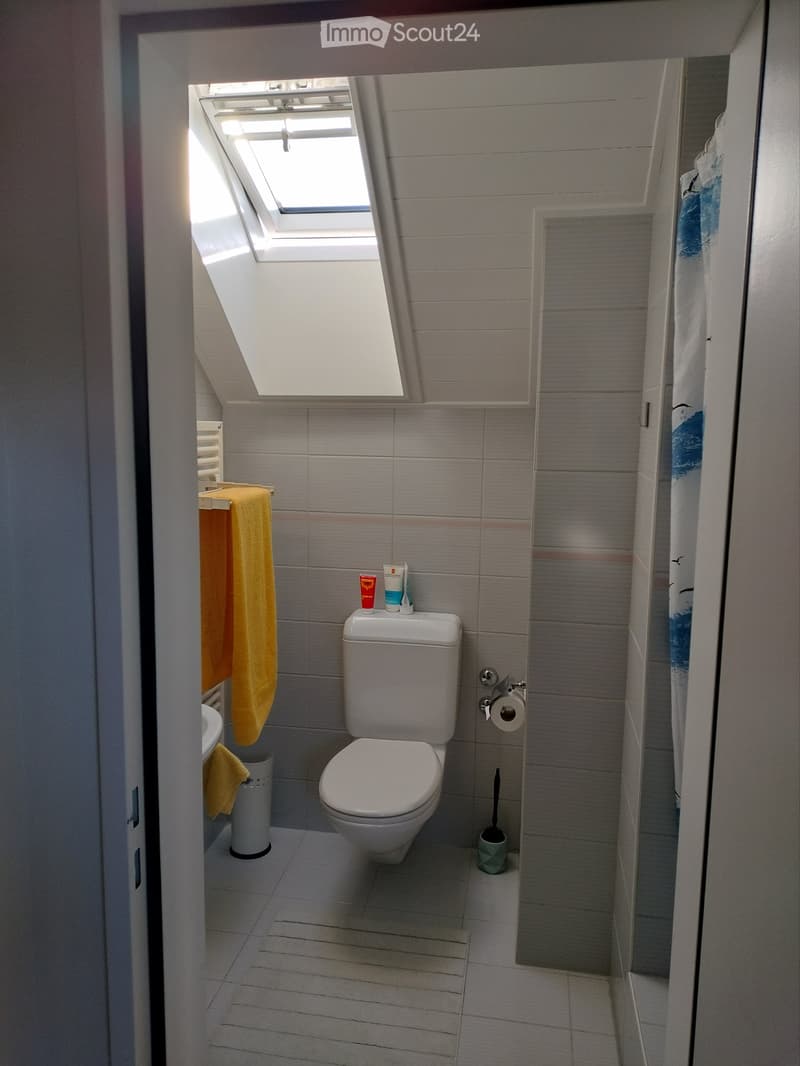 Modern bathroom with grey tiled walls, white toilet, yellow towels, and a skylight window above.