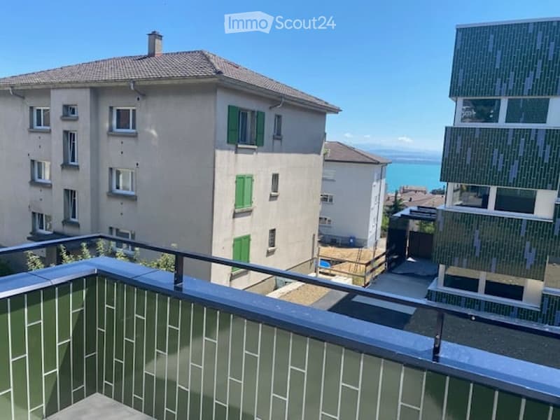 Balcony overlooking a residential area with multiple buildings, green shutters, and a distant lake view.