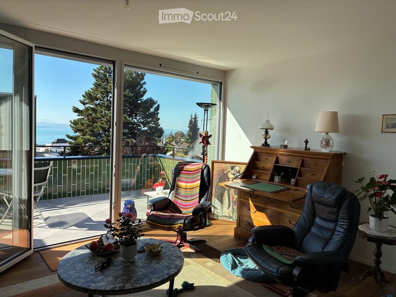 Bright living room with large windows offering a scenic view, furnished with a sofa, chairs, a coffee table, lamps, and a desk.