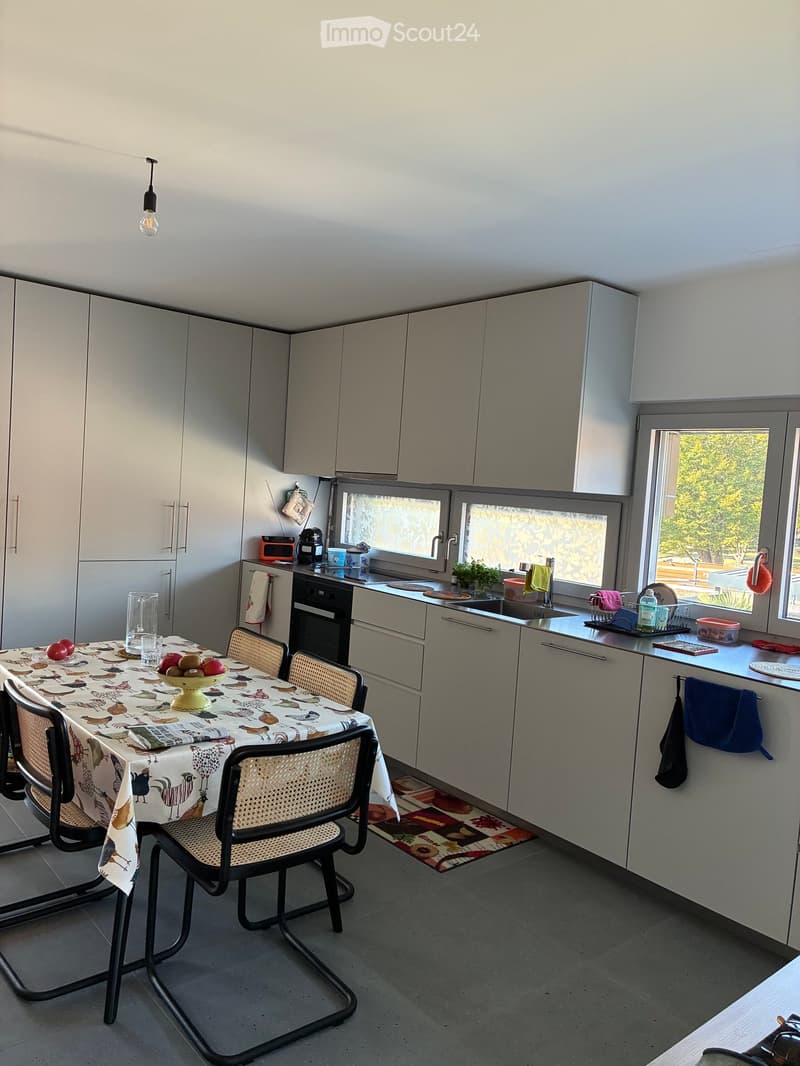 Modern kitchen with white cabinets, a dining table with chairs, and various appliances including an oven and sink.