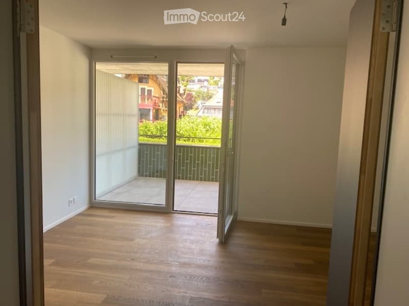 Empty room with wooden flooring, large sliding glass doors leading to a balcony, and white walls.