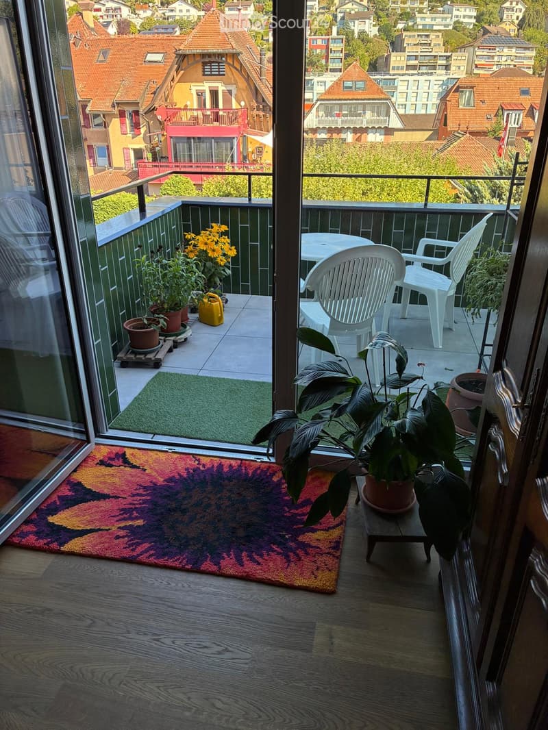 Balcony with a view of the city, featuring a table, chairs, and potted plants.