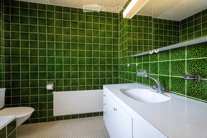 Bathroom with green patterned tiles, white sink, toilet, and radiator.