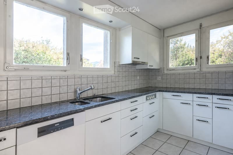 Modern kitchen with white cabinets, granite countertop, stainless steel sink and faucet, and built-in dishwasher. Large windows provide natural light.