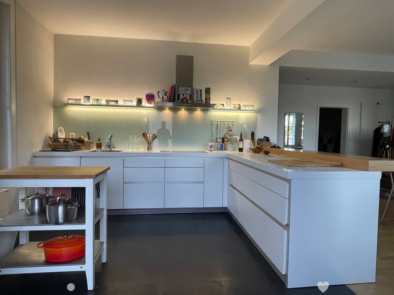 Modern kitchen with white cabinets, island, sink, and various kitchen items including pots, pans, and bottles.