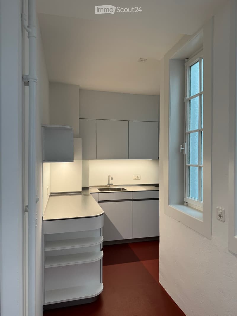 Modern kitchen with white cabinets, a sink, and a window. The floor is red, and the walls are white.
