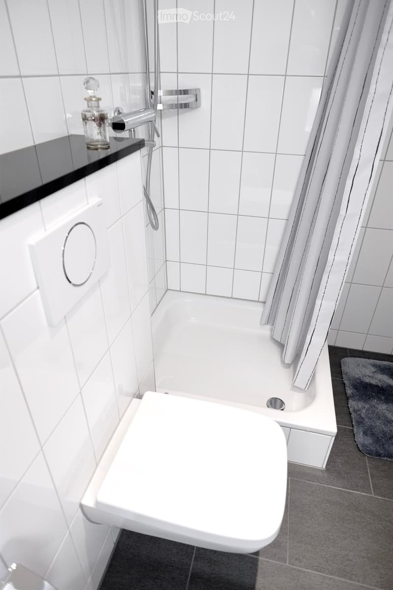 Modern bathroom with white tiles, a bathtub, a shower area with a glass enclosure, a sink with a modern faucet, and a decorative bottle on the sink counter.