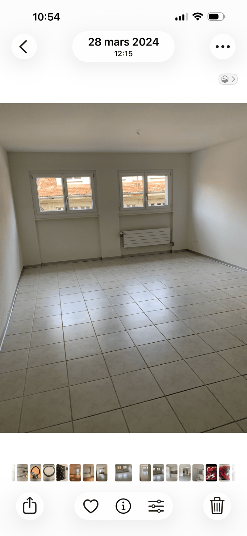 Empty room with tiled floor, white walls, and two windows showing a tiled roof view outside.
