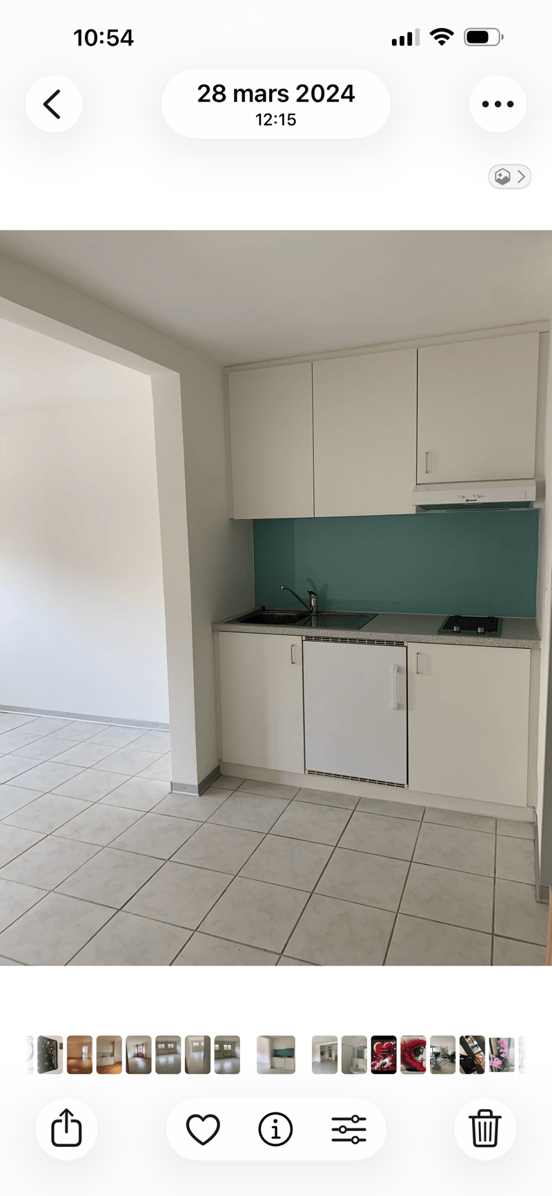Empty kitchen with white cabinets, a sink, and tiled flooring. No appliances or furniture are present.