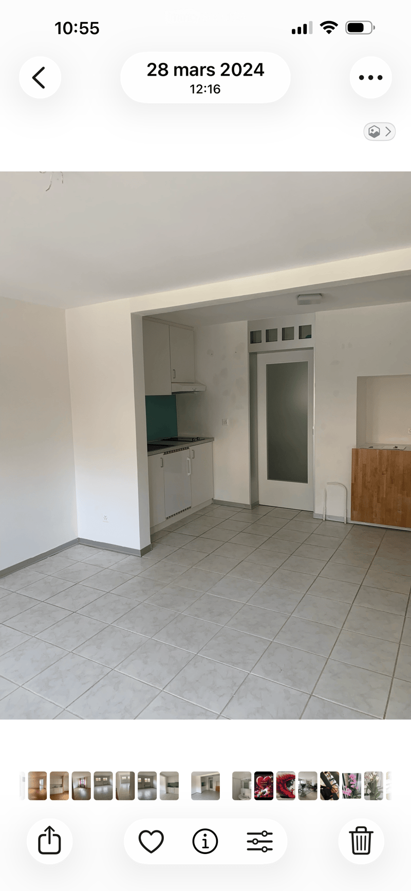 Empty room with tiled floor, white walls, and a small kitchen area with cabinets and a countertop.