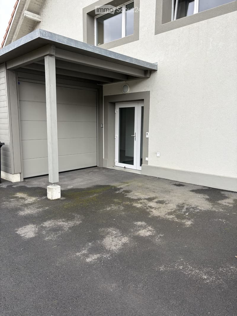 Single story building with a carport and garage. The driveway has a concrete floor.
