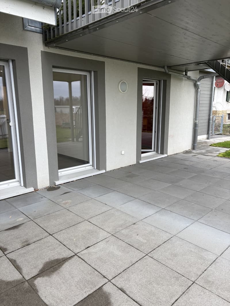 patio with floor tiles, two glass doors, two windows, balcony, metal railing, wall with gray paint, and metal fencing